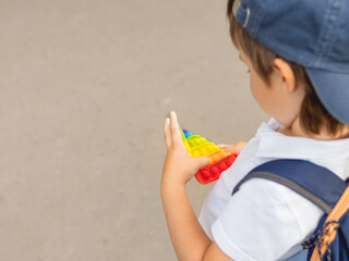 Little boy plays square rubber fidget toy Pop It. Rainbow-colored anti stress and tactile toy for all ages. Outdoor recreation with toy for fine motor skills improvement.