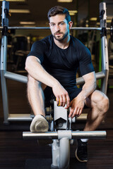 Fototapeta na wymiar athletic man rest on machine while taking a break at workout between sets and look at camera