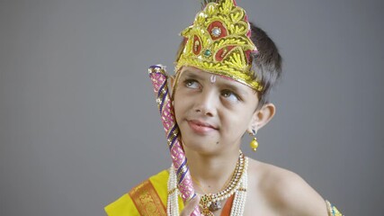 little Krishna thinking by holding flute in hand on gray background during shri krishna Janmashtami.