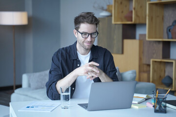 Young handsome german man wearing glasses working on laptop computer remotely from home