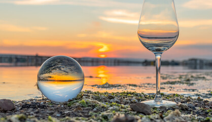 Verre à vin et boule de cristal sur fond d'étang au coucher de soleil.	