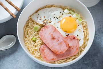 White bowl with Hong Kong breakfast made of ramen, fried egg and meat, middle close-up, elevated view