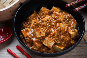 Black bowl with chinese mapo tofu made of tofu cubes, ground pork and sichuan peppercorns, closeup, studio shot