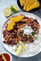 Chilli con carne or spicy meat and beans stew served with rice and nachos chips, vertical shot, middle close-up