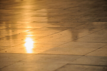 The marble floor of the city square reflects sunset sunlight