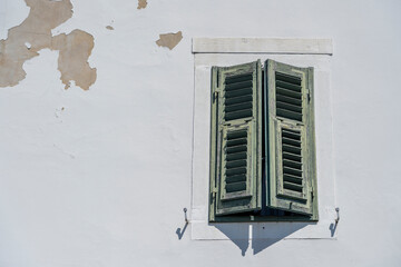 Window with green wooden shutters on old white stucco wall and copy space