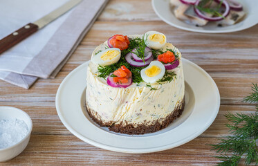 Snack, round Swedish salad cake with herring, potatoes, egg and sour cream mousse on black bread on a light plate on a wooden background. Christmas and Easter recipes.