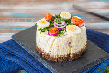 Snack, round Swedish salad cake with herring, potatoes, egg and sour cream mousse on black bread on a slate or stone board on a wooden background. Christmas and Easter recipes.