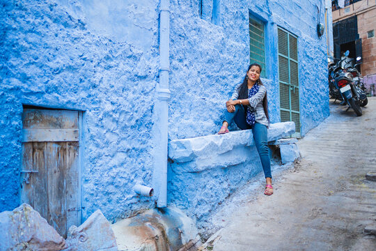 Beautiful Indian female model at blue district Chandpole of the old city in Jodhpur, Rajasthan, India. Attractive girl with long hair in modern clothes, blue jeans and blue background. 