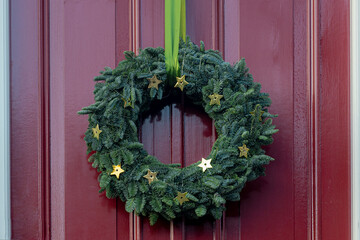 Season greeting theme, Christmas wreath made from green pine tree assortment of flowers hanging on front door, Xmas ring decoration with on wooden background.