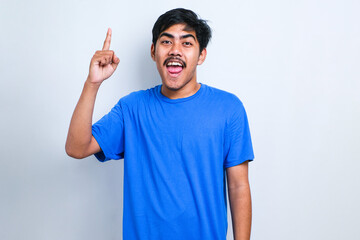 Fototapeta premium Asian man wearing casual t-shirt pointing finger up with successful idea. Exited and happy. Number one.