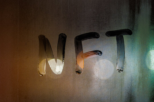 the word NFT - non-fungible token handwritten on foggy window glass at night