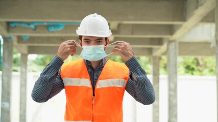 portrait of worker man wearing protective face mask in construction site during Coronavirus or Covid 19 pandemic  outdoors .engineer putting medical mask on face against air pollution . slow motion