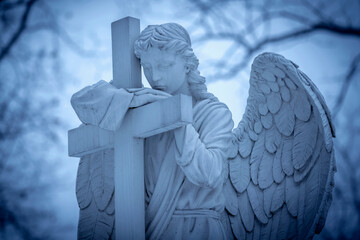Dramatic view of beautiful delicate angel with cross as symbol of human death and end of life.