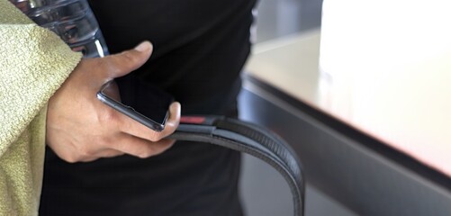 An unrecognizable young man holds a towel, a bottle of water, a smartphone and a strength belt while entering a gym