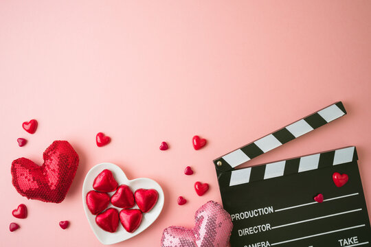 Happy Valentines day and romantic movie concept with  movie clapper board, heart shapes and chocolates on pink background. Flat lay, top view