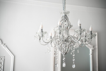 A beautiful expensive chandelier with many crystal crystals is hanging near a white wall.