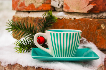Green set cup with a saucer with black coffee near the Christmas tree artificial branch in the snow 
