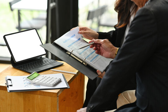 Cropped image of an insurance agent offering a life insurance choice to the elderly customers at the working desk surrounded by a digital tablet and document.