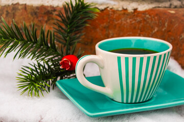 Obraz na płótnie Canvas Green set cup with a saucer with black coffee near the Christmas tree artificial branch in the snow 