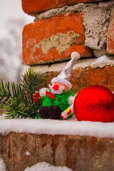 New Year's grandfather with a Christmas tree branch in the snow near the bricks