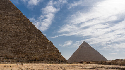 Fototapeta na wymiar Two ancient Egyptian pyramids: Cheops and Chephren on a background of blue sky and clouds. The masonry walls are visible. There are horse-drawn carts at the foot. Egypt