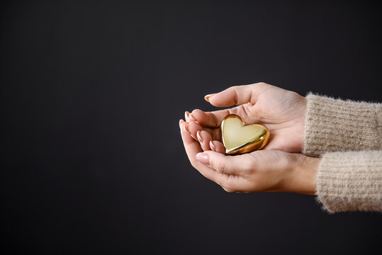 A golden heart in women's palms on a dark background