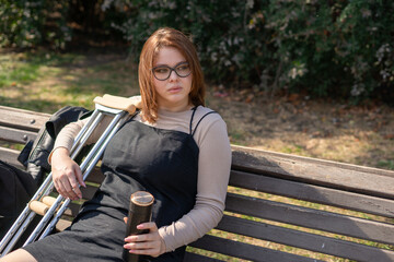 Young girl with a plastered foot in the orthosis and with crutches on a walk in the city