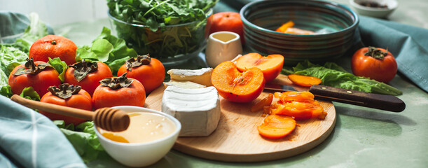 Ingredients and the process of making a vitamin winter salad with persimmons, tangerines and cheese. Selective focus Vegan salad preparation. Healthy eating. Banner
