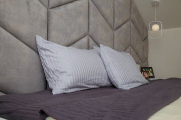 Beautiful grey bedroom, bed, pillows, soft fabric headboard. Modern interior design, close up shot