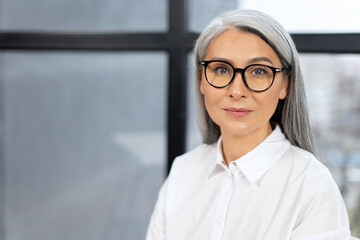 Portrait view of confident and smiling old senior business woman wearing glasses looking at the camera with pleasure smile. Employee worker sitting at the office concept