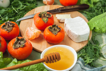 Ingredients and the process of making a vitamin winter salad with persimmons, tangerines and cheese. Selective focus