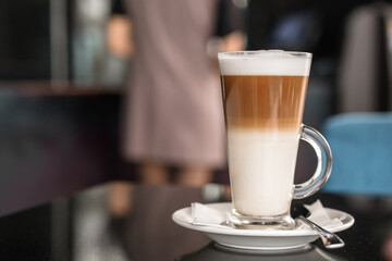 A glass of coffee latte on a table against a blurred background.