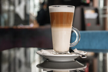 A glass of coffee latte on a table against a blurred background.