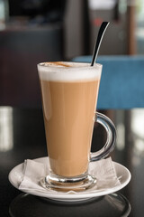 A glass of coffee latte on a table against a blurred background.