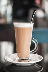 A glass of coffee latte on a table against a blurred background.