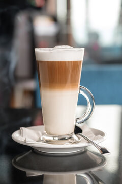 A glass of coffee latte on a table against a blurred background.