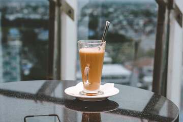 A glass of coffee latte on a table against a blurred background.