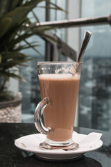 A glass of coffee latte on a table against a blurred background.