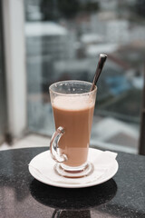 A glass of coffee latte on a table against a blurred background.