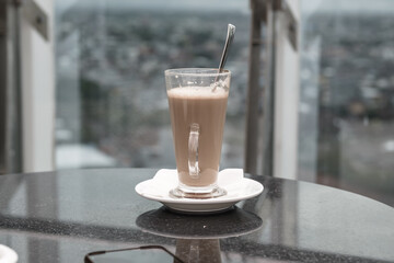 A glass of coffee latte on a table against a blurred background.