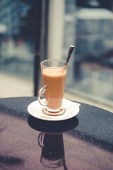 A glass of coffee latte on a table against a blurred background.