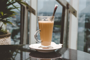 A glass of coffee latte on a table against a blurred background.