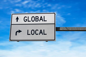 Road sign with words global and local. White two street signs with arrow on metal pole on blue sky...