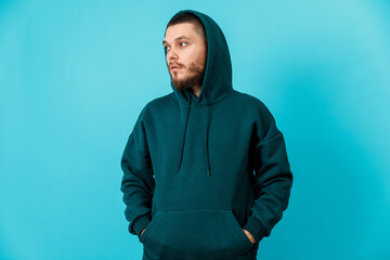 handsome young man with a beard in a green tracksuit looking to the side on a blue background. isolated