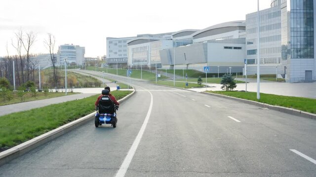 Aerial view of a man with amputated legs and arms drives on electric wheelchair along the empty street in Far Eastern Federal University campus area
