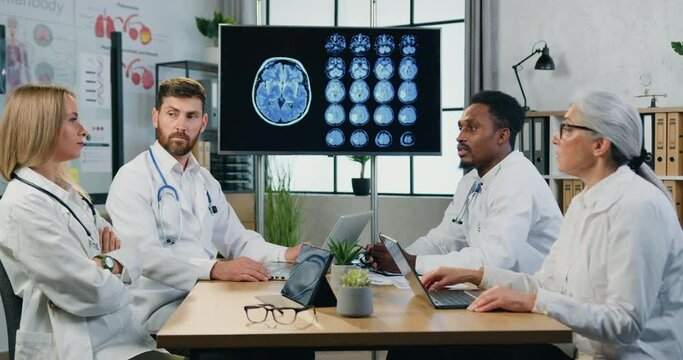 Attractive qualified responsible multiethnic male and female doctors sitting around meeting table in medical room and discussing patient's mri brain,medical concept