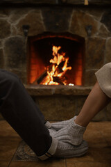 The feet of a man and a woman in warm socks next to the fireplace.
