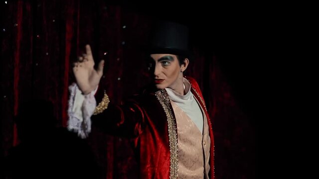 The main showman points his finger at the audience. A wizard guy with makeup in a red tailcoat is mysterious.