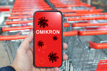 display of a mobile phone, shopping trolleys in the background. display shows covid-19 virus and...